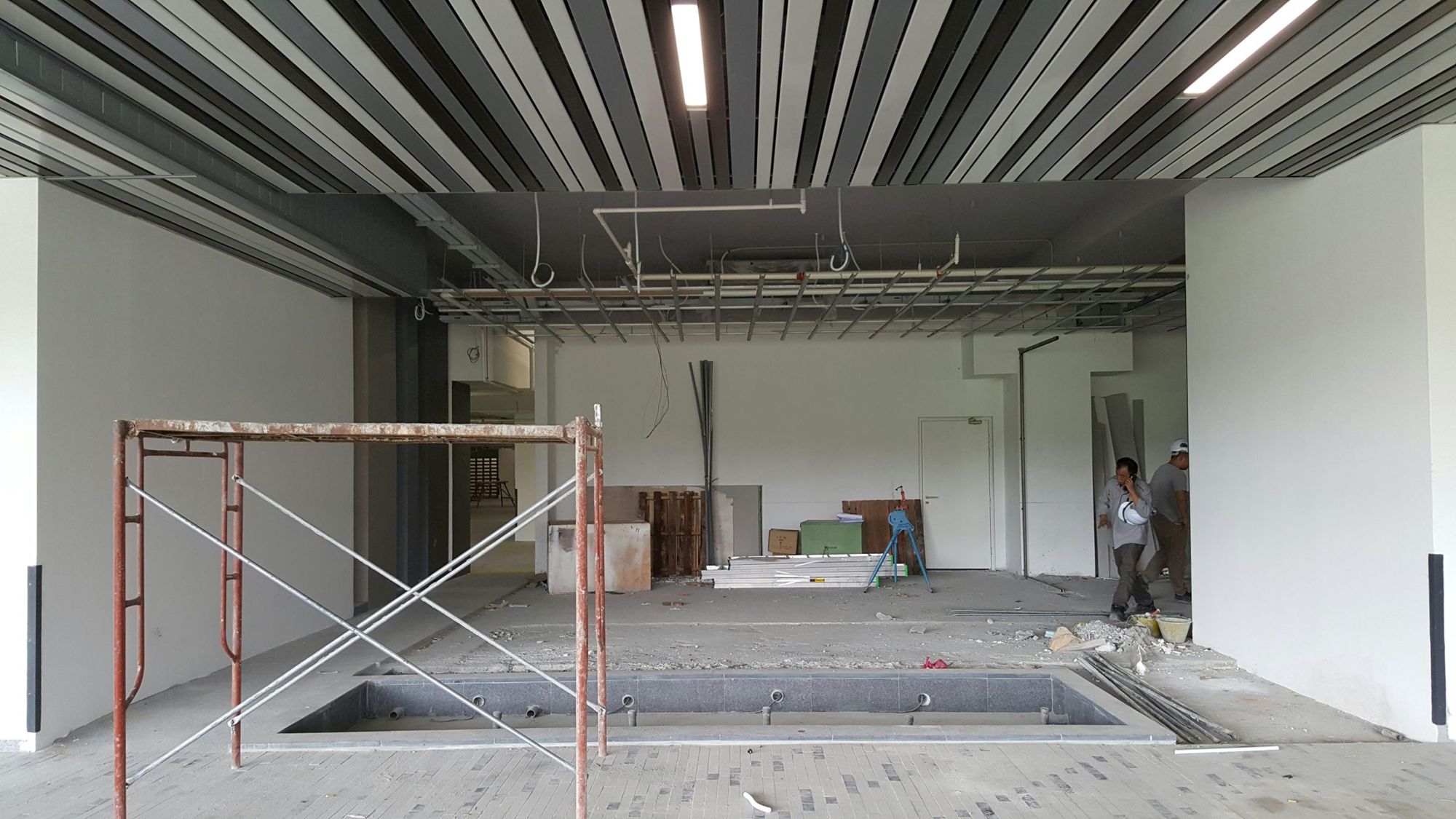 Obra em andamento com andaime, forro aberto e instalações aparentes, com profissionais conferindo o espaço