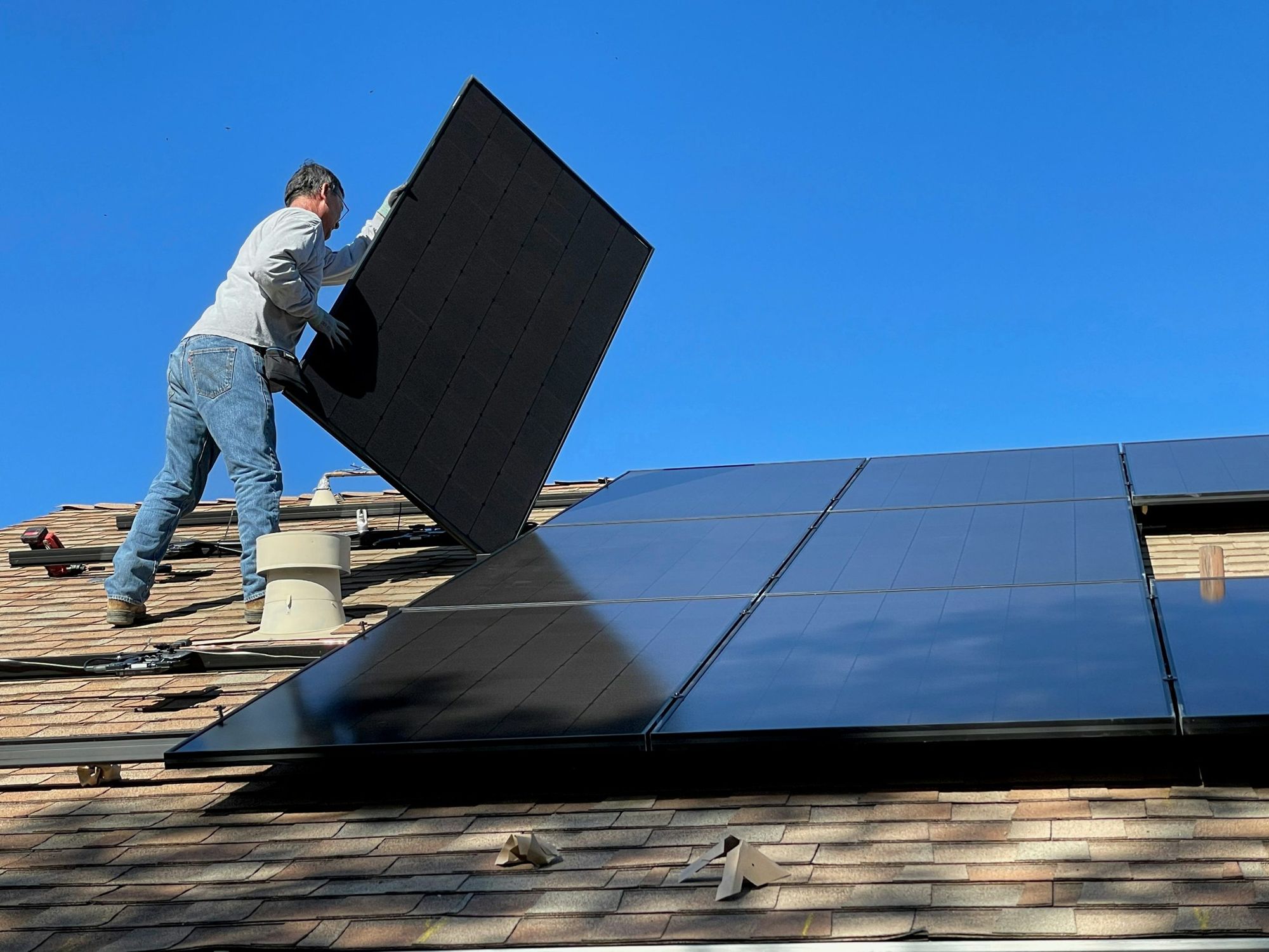Instalador colocando painéis solares no telhado de uma casa sob céu azul