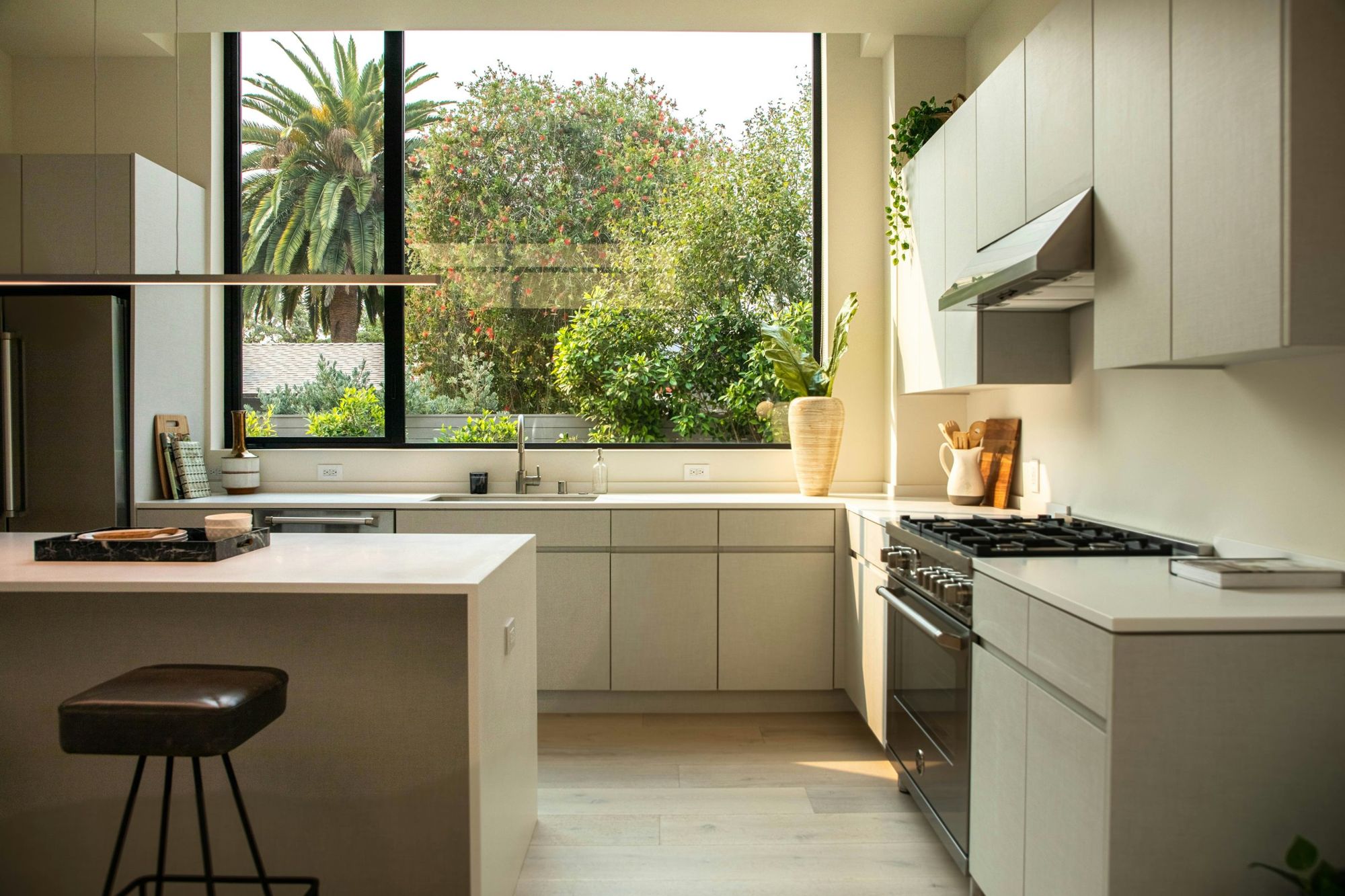 Cozinha clara com armários planejados, ilha com banqueta, fogão em inox e janela ampla para o jardim