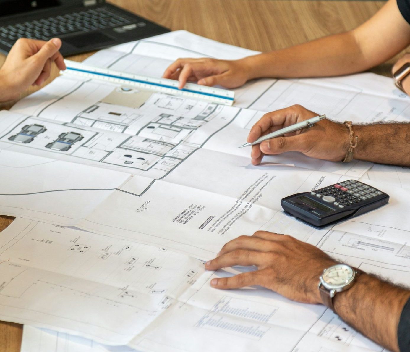 Equipe analisando a planta do projeto sobre a mesa, com régua, lapiseira e calculadora